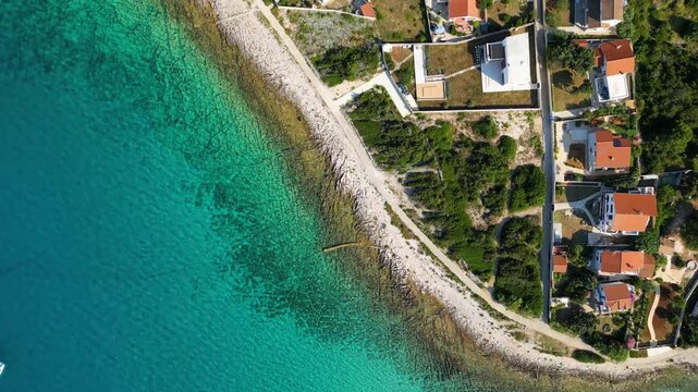 An aerial panoramic view of the tranquil turquoise bay on Silba Island, Croatia, featuring anchored sailboats along a lush, green Mediterranean coastline with charming red-roofed village houses under