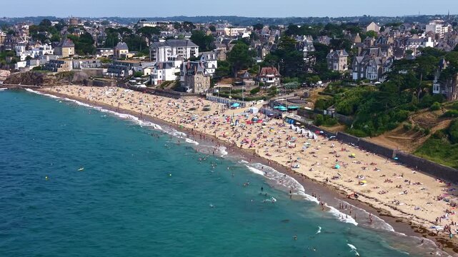 Plage de Saint-Enogat crowded with beachgoers along Dinard waterfront, coastal promenade, Belle Epoque villas and urban district, Ille-et-Vilaine, Brittany, drone pullback