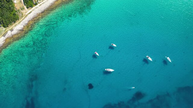 An aerial panoramic view of the tranquil turquoise bay on Silba Island, Croatia, featuring anchored sailboats along a lush, green Mediterranean coastline with charming red-roofed village houses under