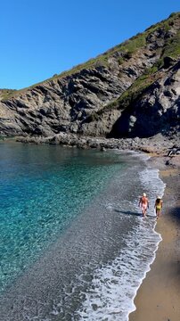 A couple enjoys the beauty of La Frana Beach in Sardinia, Italy, where turquoise waters meet golden sands. Beachgoers walk along the shore, embracing the picturesque scenery and serene atmosphere.