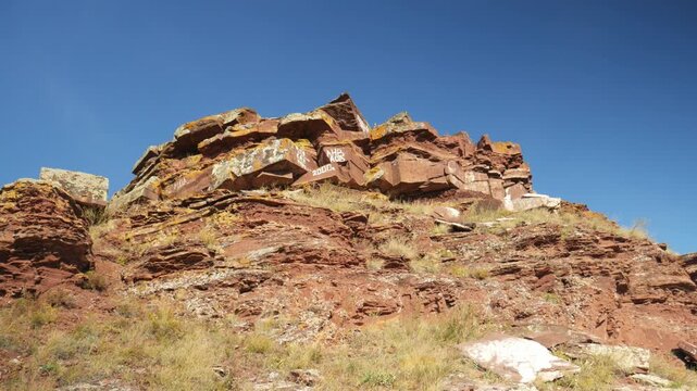 View of a Devonian red sandstone cliff marred by painted graffiti vandalism. Autumn landscape with dry grass in Khakassia, Russia under a clear blue sky.