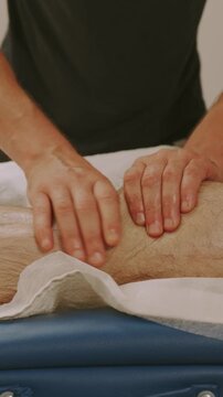 closeup shows therapist palms gliding along client's calf on blue padded clinic table towel near foot lighting
