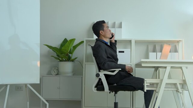 Professional man in a black blazer talking on his smartphone while working at a modern office desk
