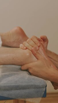close-up of hands applying steady pressure to toes and foot arch on towel-covered table, oil glow indoors