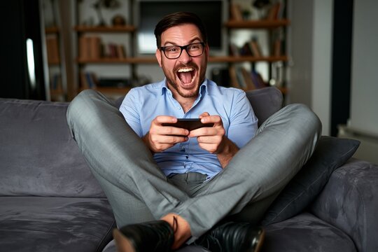 Excited man sitting on a sofa playing a game on his smartphone and laughing out loud