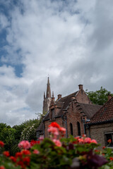 Obraz premium Bruges church spire and brick buildings with flowers