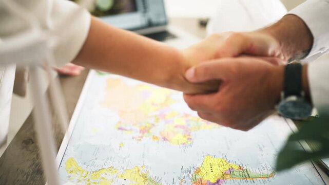 International business partners shaking hands over a world map in a global energy meeting, symbolizing a successful partnership agreement and renewable power collaboration