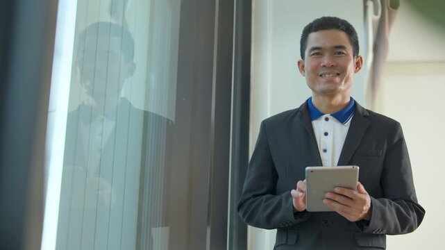 Professional man in a suit holding a tablet while standing near a large glass office window
