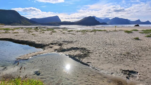 Summer landscape at Haukland Beach in the Lofoten Islands with pale sandy beach, shallow water, impressive mountains and blue sky with white clouds.