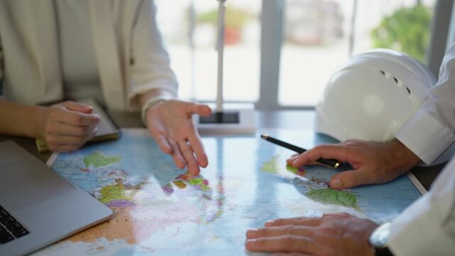 International business partners planning global expansion strategy pointing at world map during a meeting, showcasing collaboration, logistics, and supply chain management concepts