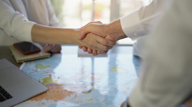 Successful travel agents shaking hands over a world map, finalizing an international tour deal and showcasing tourism partnership, business agreement, and global cooperation