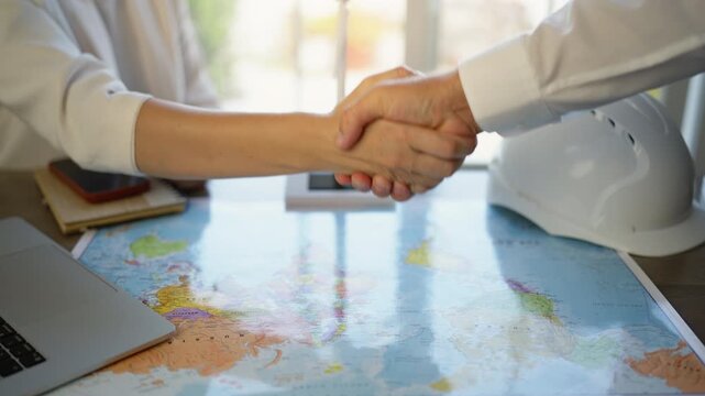 Two business partners, an engineer and an architect, shaking hands over a world map to seal an international construction agreement, symbolizing a successful global deal and partnership