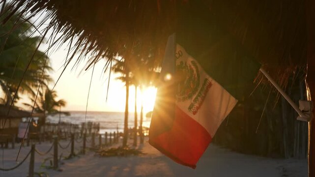 Closeup of the Mexican flag revealing golden sun rays. Beautiful sunrise in Tulum, Mexico. Footpath towards sandy beach and Caribbean sea early in the morning.