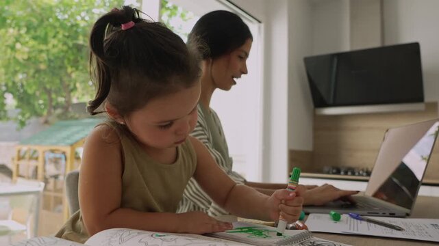 Mother working from home with daughter coloring nearby