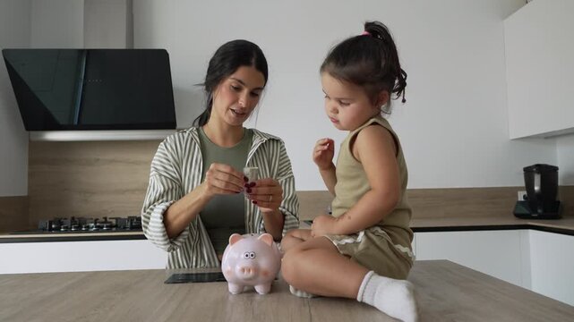 Mother teaching daughter about saving money in a piggy bank