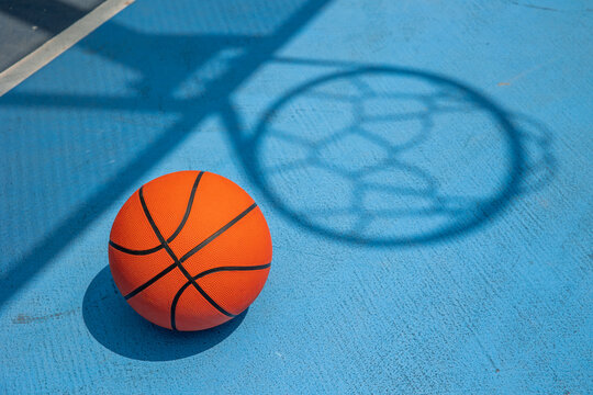 Basketball on blue court with hoop shadow