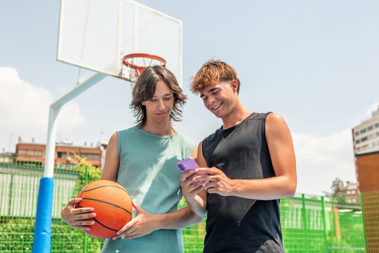 Teen friends using smartphone on basketball court