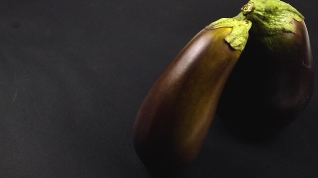 Two fresh purple eggplants are on the black table, side view, slow motion