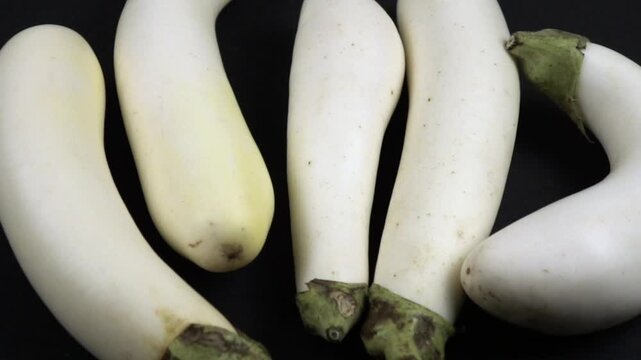 White fresh eggplants are on the black table, top view, slow motion
