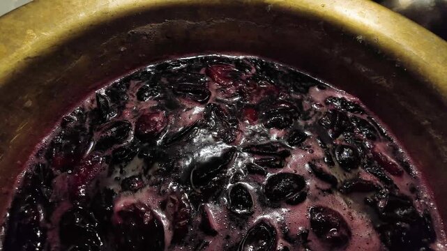 Stirring plum jam with wooden spatula in a cooper basin while cooking plum jam 