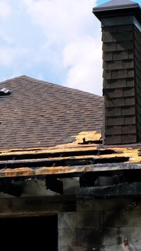 Damaged brick chimney stands on the roof of burned house. Concept of fire insurance. Arson case. Consequences of a gas or battery explosion. Home maintenance, structural repair, building inspection.