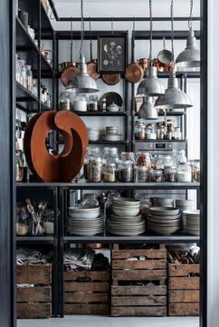 Orderly industrial kitchen with steel shelving, pendant lamps, glass jars and wooden crates