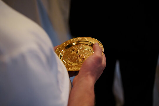 Person holding a golden communion plate during a religious service, illustrating traditional eucharist rituals and sacred church practices, sacred service, traditional worship