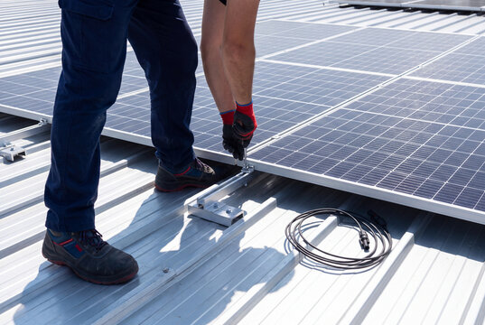 Technician Installing Solar Panels with Mounting Brackets on Corrugated Metal Roof