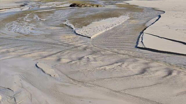 Small water channels create natural patterns and textures in the pale sand at low tide on Haukland Beach, Vestvagoya, Lofoten Islands, Norway.