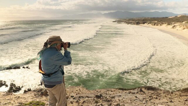 female photographer overlooking overhead view of massive wave sets rolling into Walker Bay Nature Reserve beach, South Africa