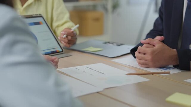 Business professionals point at data trends on a tablet screen, an Apple Pencil in hand, capturing detailed market analysis hands analyzing stock market charts on a tablet, colleagues gathered around