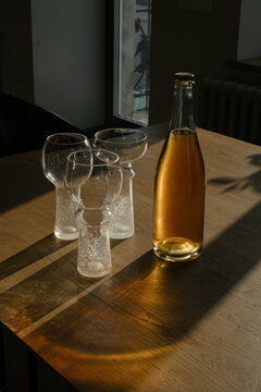Glass bottle of craft apple cider and elegant empty glasses on a wooden table. Hard shadows, minimalist lifestyle and beverage concept.