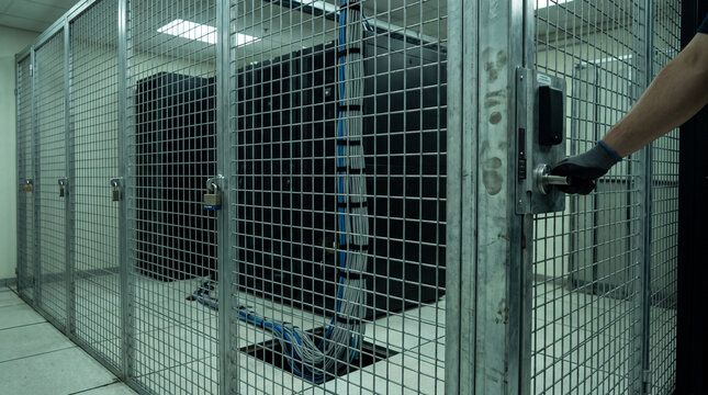Secure Server Room Access: A gloved hand reaches for the lock on a caged server room, safeguarding sensitive data and advanced technology within a modern data center.