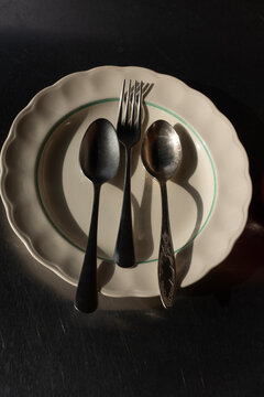 Top view of vintage spoons and fork served on a ceramic plate with shadows
