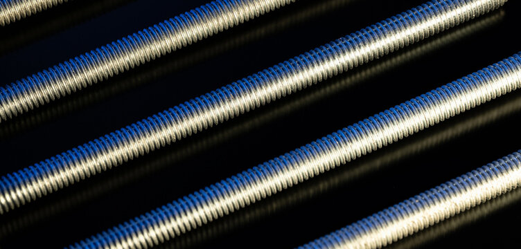 Parallel metal threaded rods showing mechanical engineering, industrial hardware, and connection concepts on a dark background