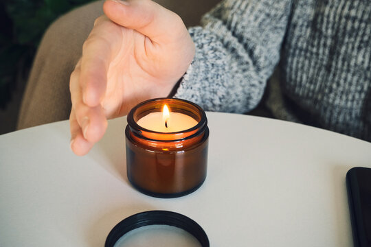 Hand near burning candle on table, creating cozy and relaxing atmosphere