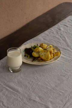 Roasted potatoes with herbs served with a glass of cold kefir on a linen tablecloth