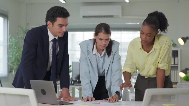 Coworkers gather around a table analyzing business reports together, capturing genuine teamwork in a welllit corporate space.