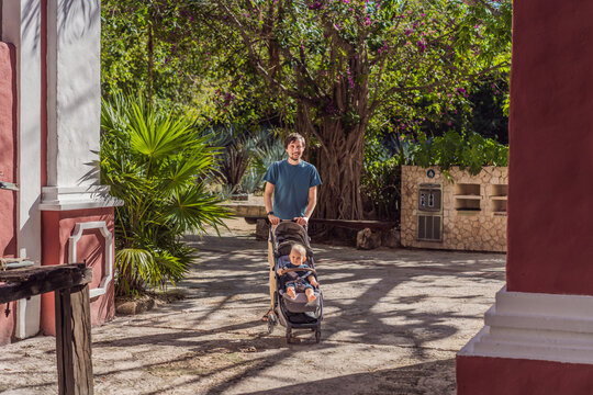 Man walking with baby stroller through Mexican colonial street, colorful architecture, heritage courtyard, fatherhood and family travel with baby concept