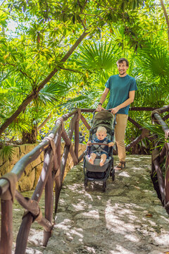 Dad walks with an infant stroller through dense tropical greenery, showing family travel, fatherhood, eco park visit and vacation routine concept