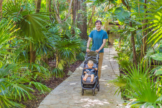 Dad walks with an infant stroller through dense tropical greenery, showing family travel, fatherhood, eco park visit and vacation routine concept