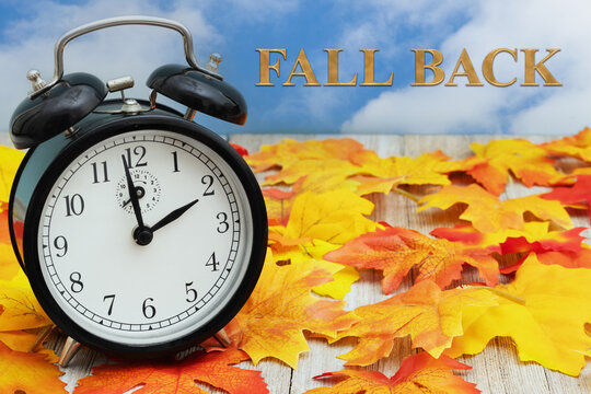 DST daylight saving time with Fall back with fall leaves and alarm clock on wood bench with sky