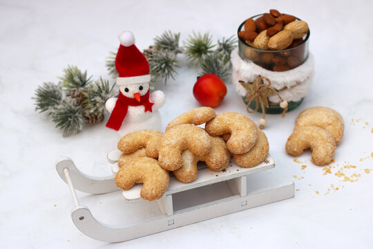 Traditional vanilla crescent cookies on a white decorative wooden sled with a snowman and nuts against a light-colored background.