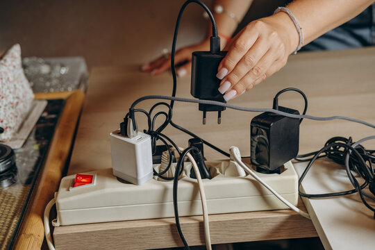 Woman Plugging Multiple Chargers Into Power Strip With Tangled Cables And Adapters