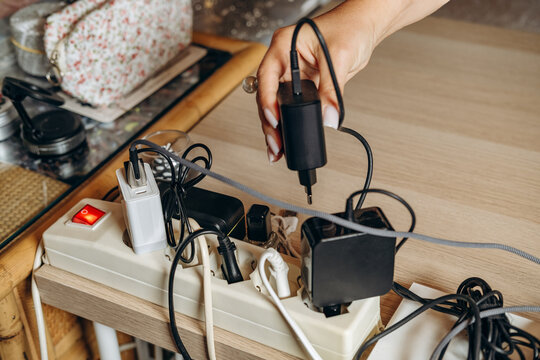 Woman Plugging Charger Into Overloaded Power Strip on Cluttered Desk With Tangled Cables