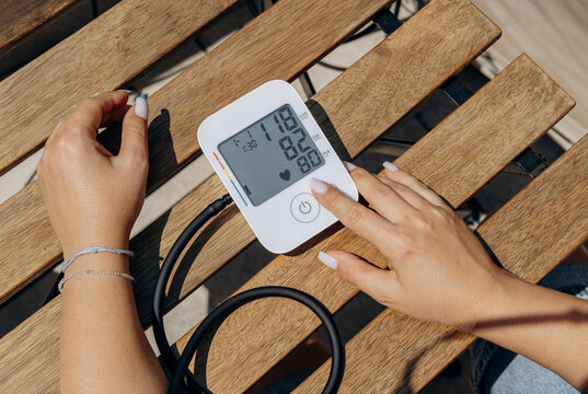 Woman Checking Blood Pressure With Digital Monitor On Wooden Bench Outdoors For Home Health