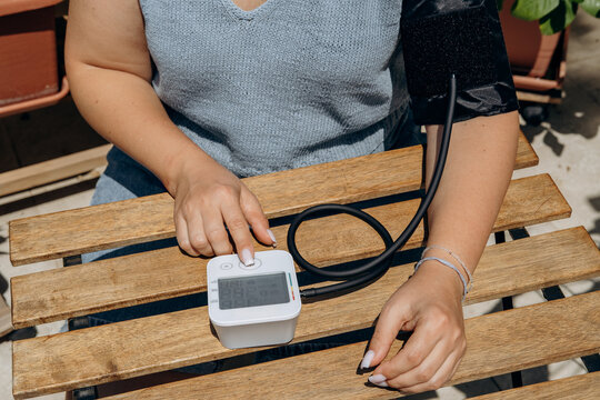 Woman Checking Blood Pressure at Home With Digital Arm Cuff Monitor on Wooden Table