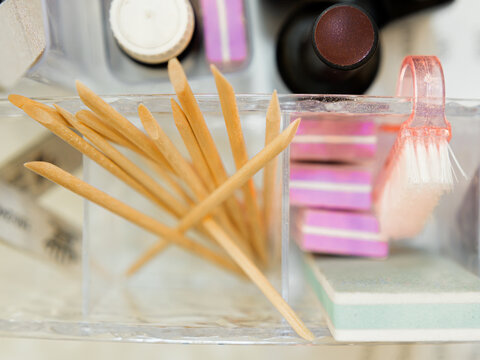 A horizontal top-down view of wooden cuticle sticks and nail buffers arranged in a clear organizer on a salon desk.   