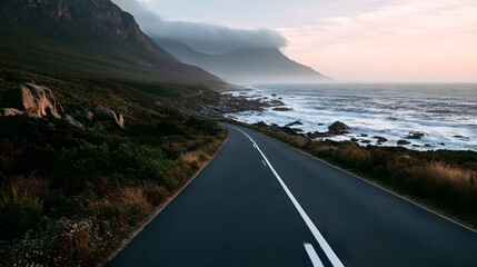 Obraz premium A winding coastal road curves along rugged cliffs beside crashing ocean waves under soft morning light