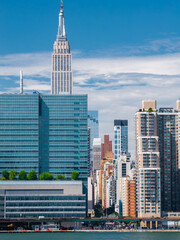Fototapeta premium Empire State Building rises over modern waterfront glass skyscrapers and highway traffic in Manhattan, New York City on a bright summer day.